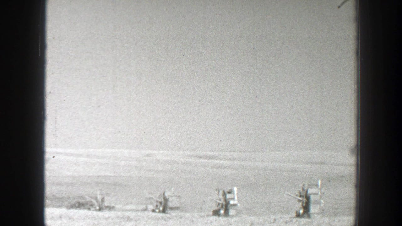 Distant equipment or vehicles lined across a flat plain beneath a pale sky.