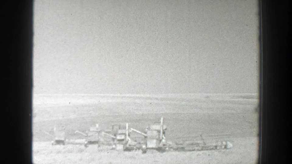 Soft black-and-white home-movie frame showing distant equipment or vehicles across a flat California landscape in 1939.