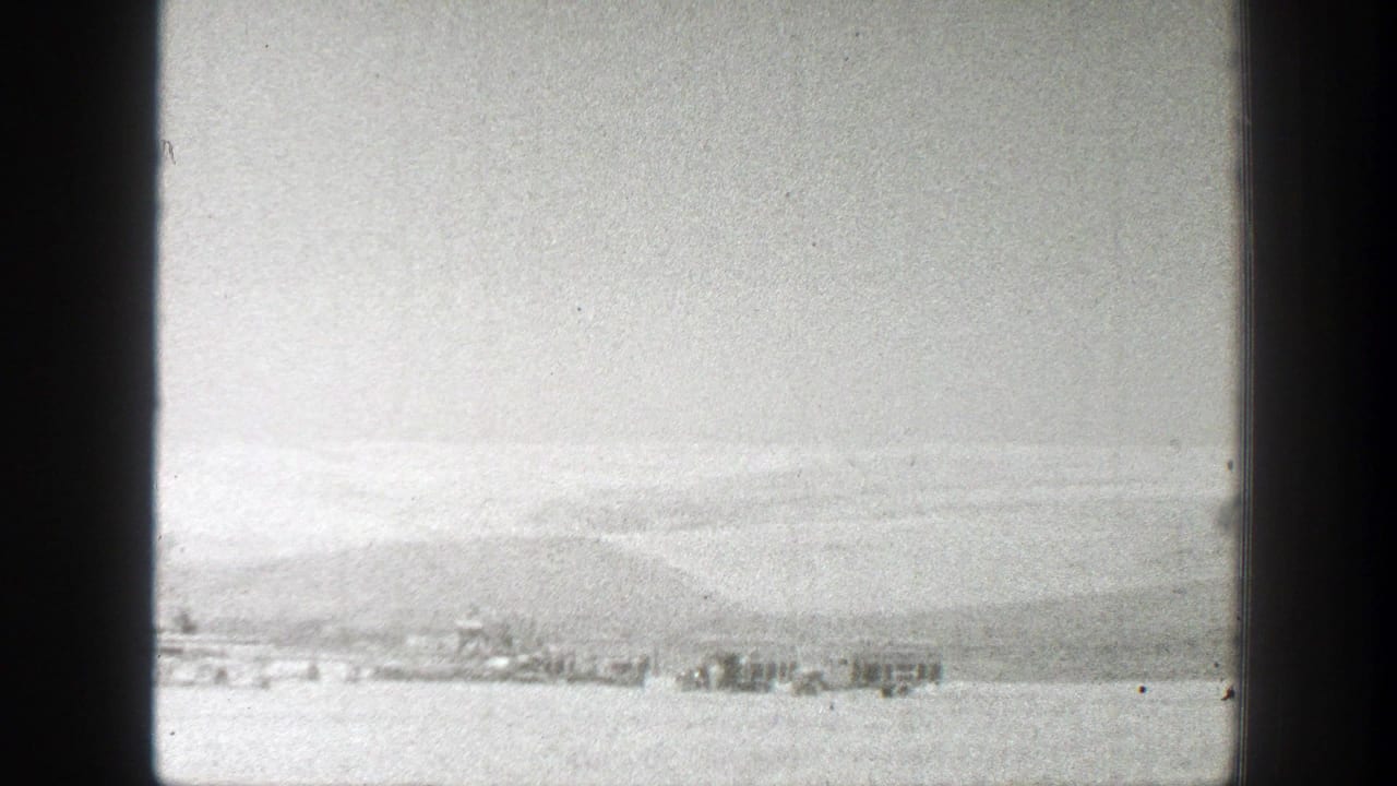 1939 California 8mm frame showing a distant shoreline or water view, low hills, bright sky, and small structures near the horizon.
