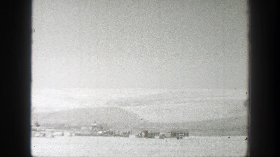 1939 California 8mm frame showing a distant shoreline or water view, low hills, bright sky, and small structures near the horizon.