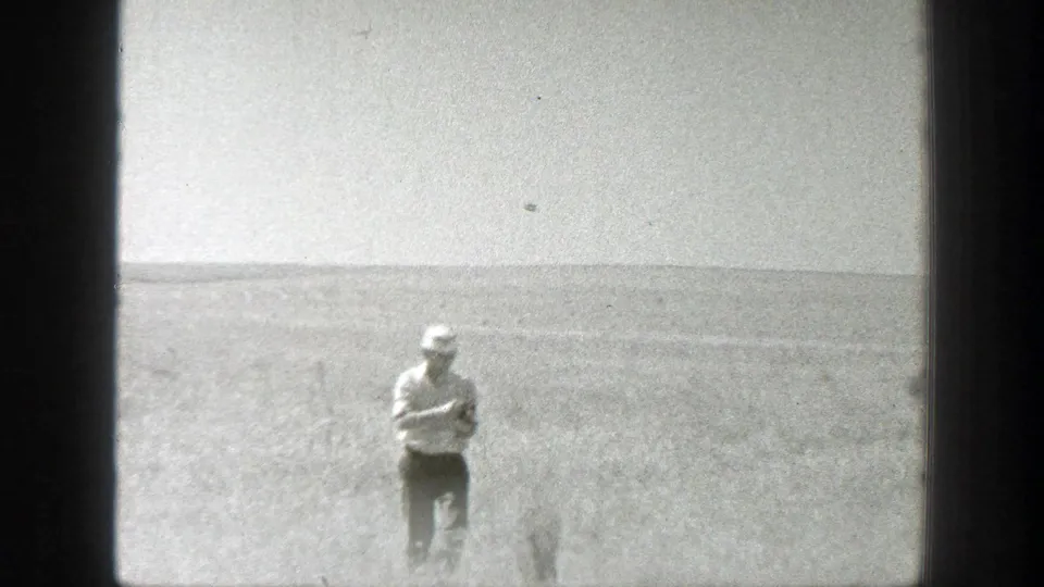 1939 California 8mm frame showing a man in a white hat and light shirt standing in a wide open field beneath a bright sky.