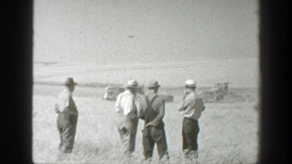 Four men in hats and overalls stand in a sunlit California field in 1939 home-movie footage, with machinery visible in the distance.