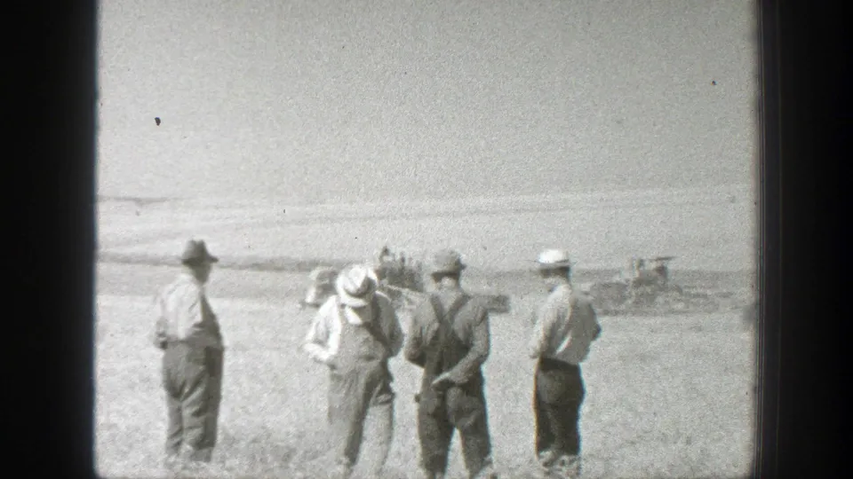 Men in hats stand and face one another in a 1939 California field, with soft 8mm detail and distant equipment behind them.