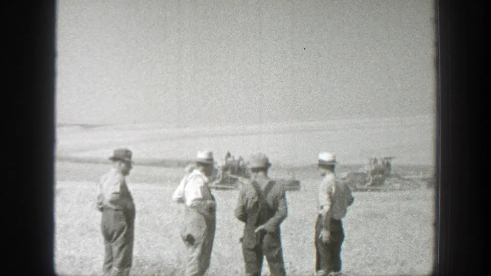 Several men in work clothes stand together in a sunlit 1939 California field, framed by open sky and distant farm equipment.
