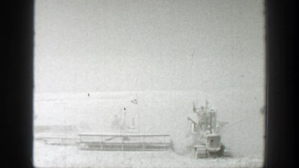 The 8mm frame shows harvesting machinery with a long horizontal platform or blade area in an overexposed California field.
