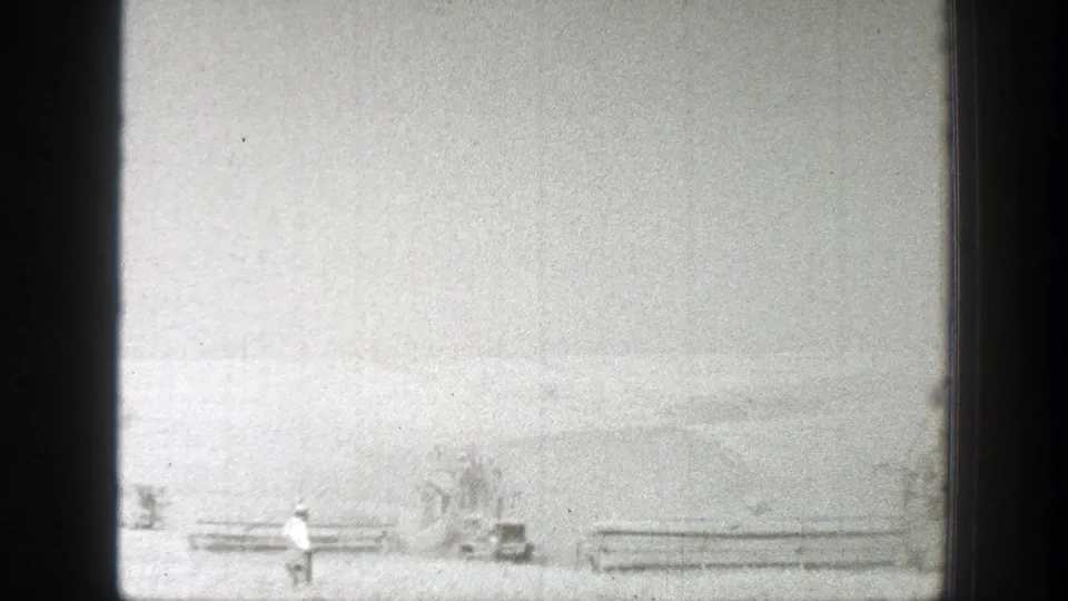 1939 California field view with a lone walking figure near distant harvester machines and low crop rows.