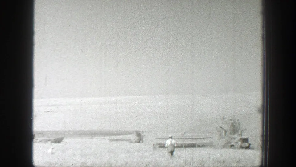 1939 California 8mm frame with a distant worker near crop rows and harvesting machinery in a sunlit field.
