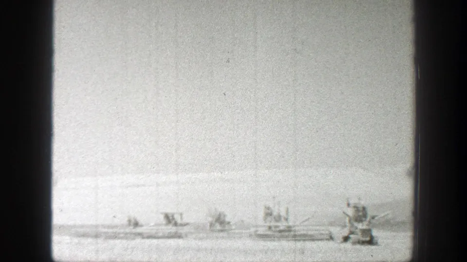 1939 California 8mm frame showing distant tractors or harvest equipment moving across a flat agricultural field.
