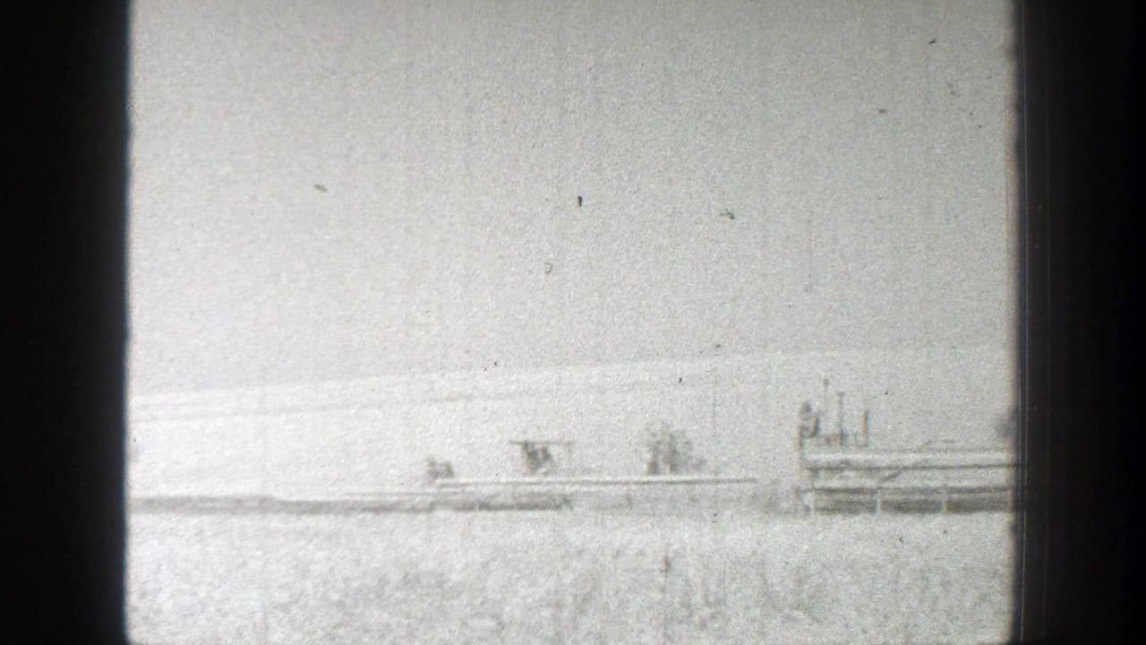 1939 California 8mm frame showing distant combines and workers spread across a wheat field during harvest.