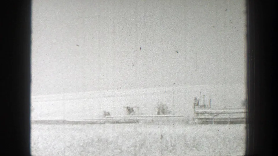 1939 California 8mm frame showing distant combines and workers spread across a wheat field during harvest.