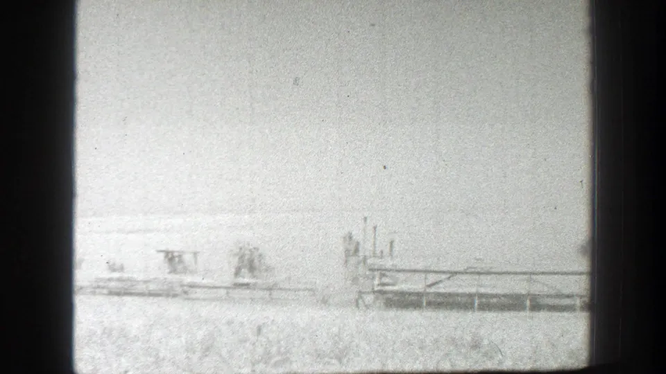 Distant view of combines and workers in a California wheat field, softened by exposure and 8mm film grain.