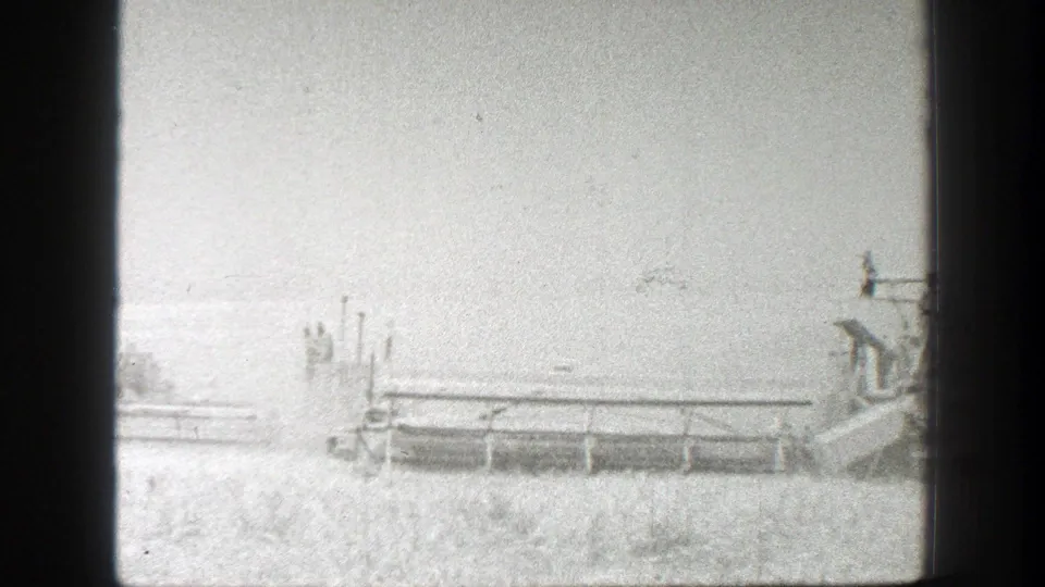 California wheat harvest frame with a combine near the right edge and additional machinery stretching across the field.