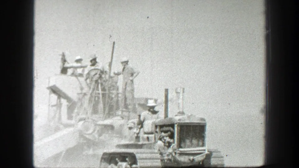 California 1939 home-movie frame showing men around heavy construction machinery, including a front grill or radiator and upright pipes.