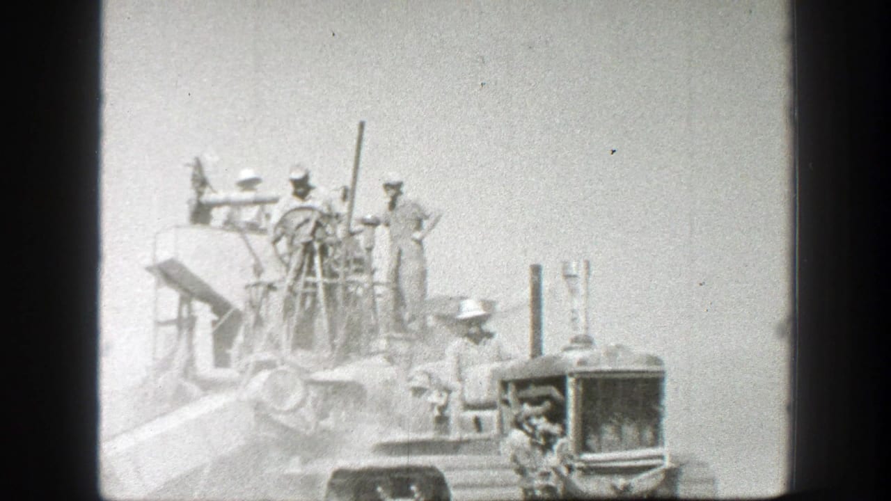 1939 California 8mm frame showing men in work hats gathered on and beside a farm tractor in an open field.