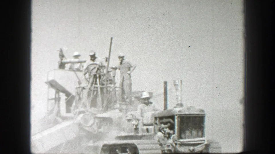 1939 California 8mm frame showing men in work hats gathered on and beside a farm tractor in an open field.