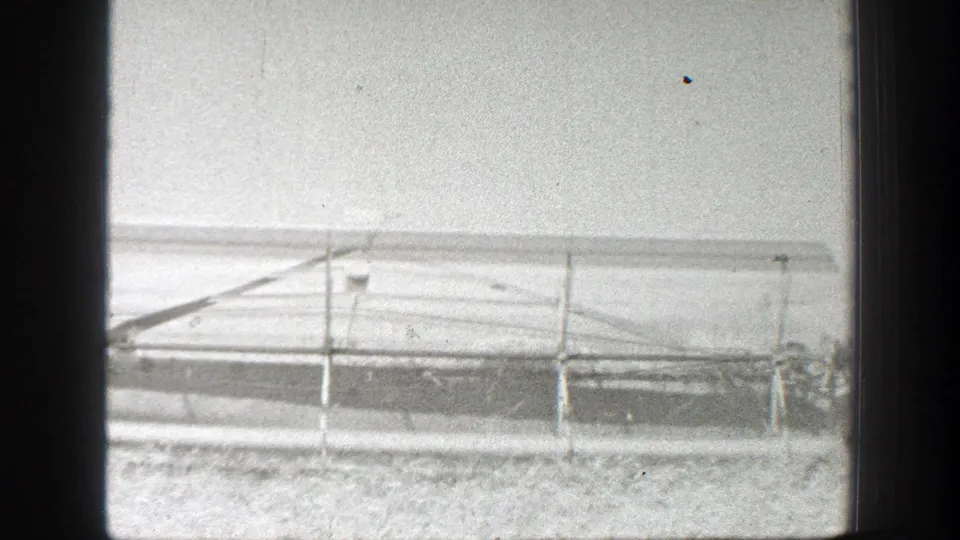 1939 California 8mm frame showing a long agricultural implement across an open field, with indistinct activity near the right edge.