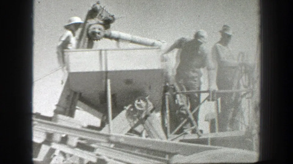 Workers in hats operate or observe a large agricultural machine on a California farm in 1939 home-movie footage.