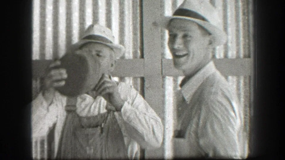 Black-and-white 8mm frame from California in 1939 showing a man drinking from a jug as another hat-wearing man smiles nearby.