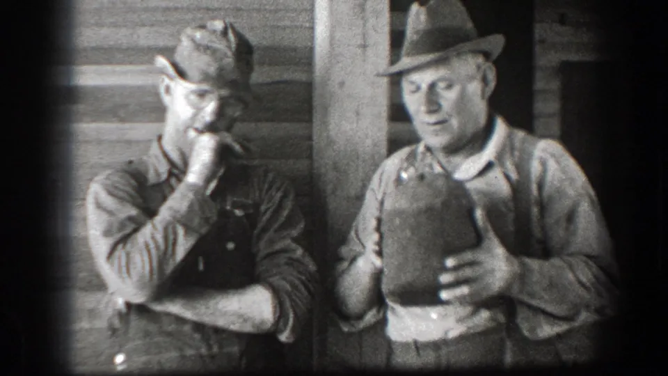 In the final frame, one man holds the jug close while his companion stands beside him near the doorway of the wooden building.