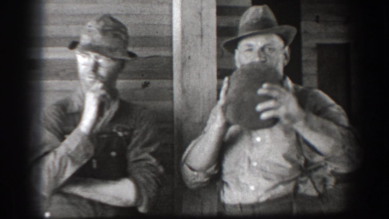 Two adult men in brimmed hats stand by a wooden structure, with one drinking from a jug.