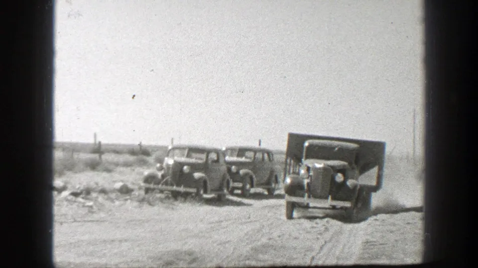 Vintage 1930s trucks appear on a dusty California dirt road with open land and utility poles in the distance.