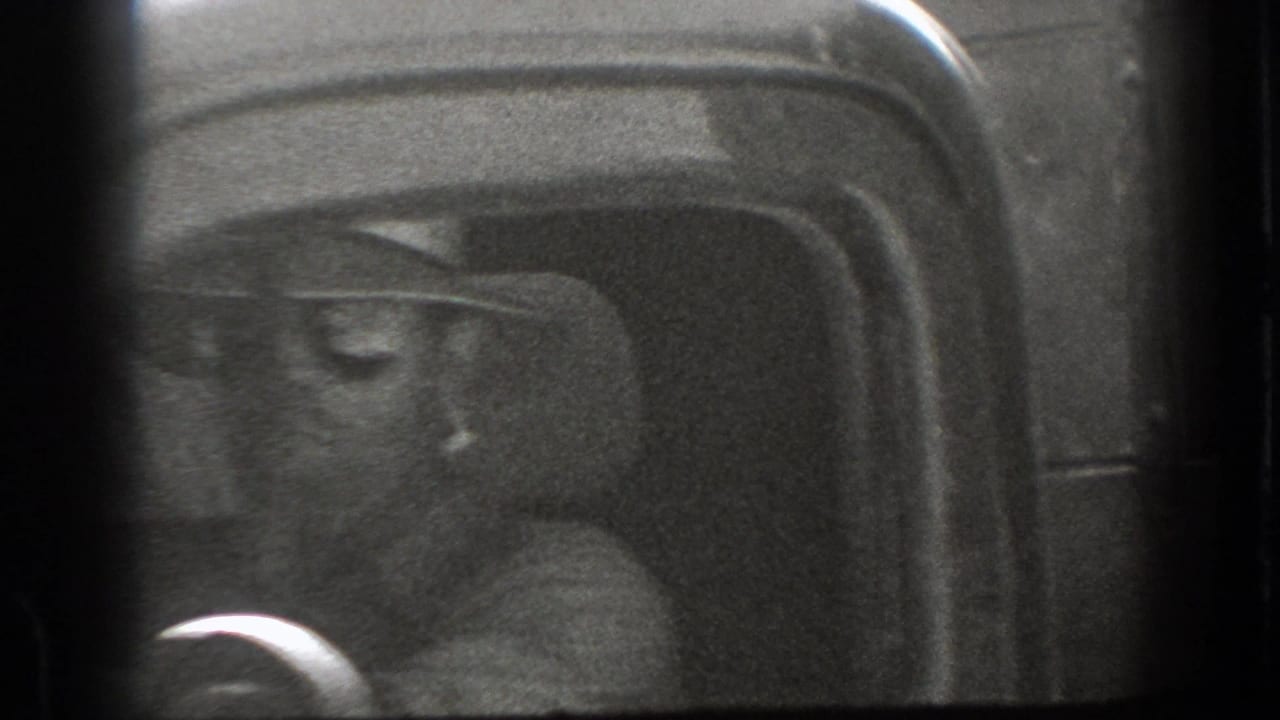 1939 California 8mm frame showing a smiling driver in a wide-brimmed hat, partly obscured by the dark interior frame of a vehicle.