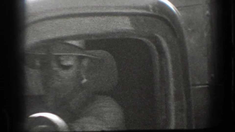 1939 California 8mm frame showing a smiling driver in a wide-brimmed hat, partly obscured by the dark interior frame of a vehicle.