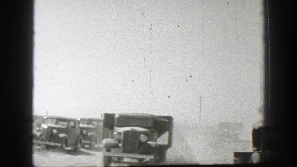 Two vintage trucks appear on a dusty California dirt road under a bright overexposed sky, with dark film or vehicle framing at the edges.