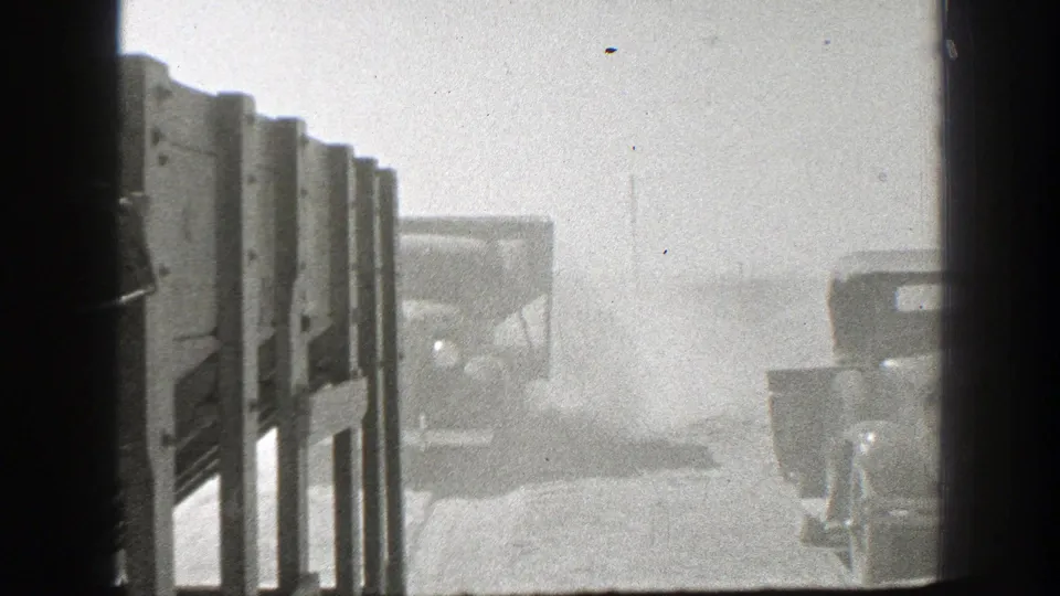The final 1939 California frame shows truck bodies along a dusty dirt road, seen through dark vertical framing and heavy roadside haze.
