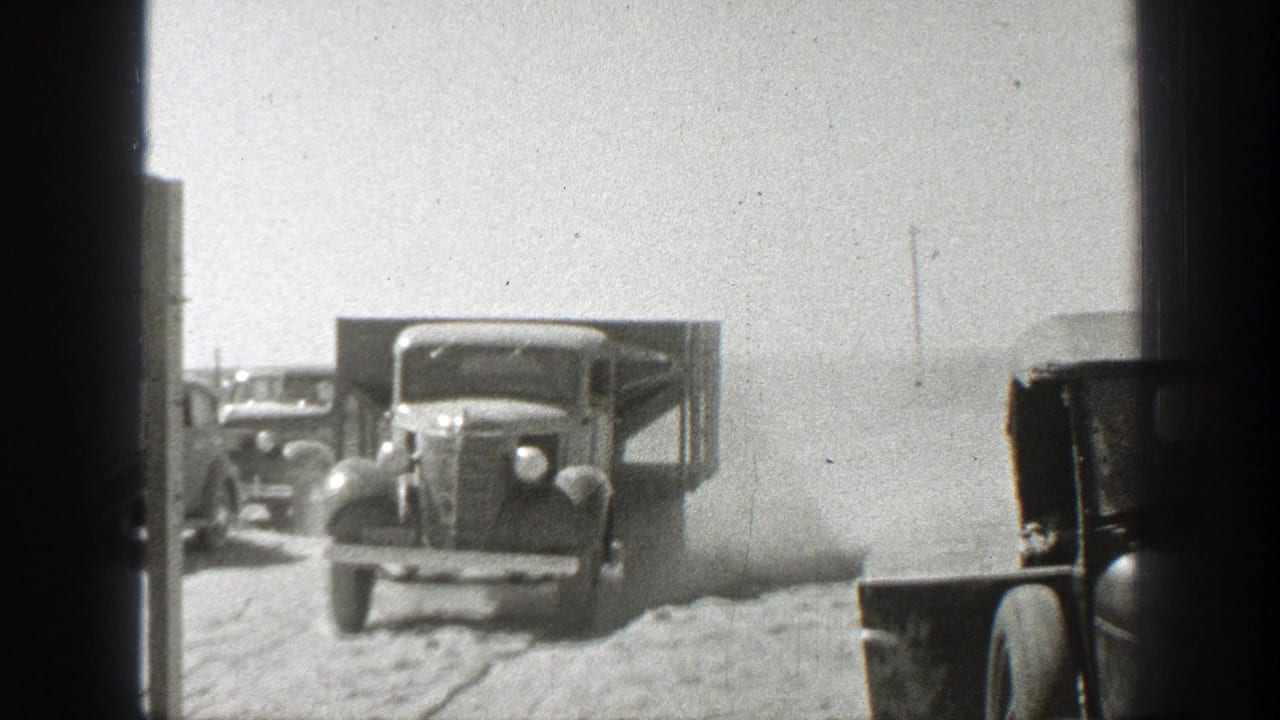 Older trucks on a dusty dirt road, seen through dark film-frame edges.