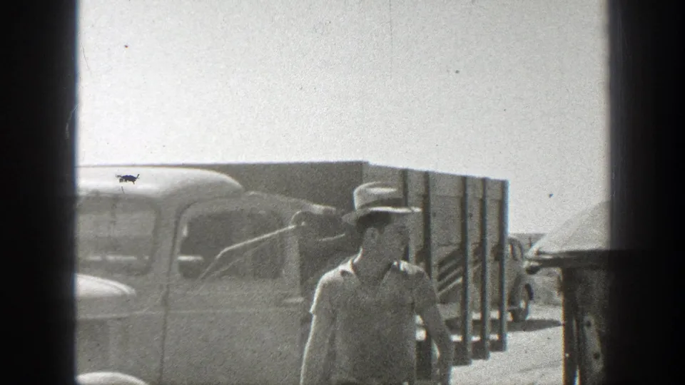 1939 California home-movie frame with a man in a hat walking near a period truck on a dusty roadside.
