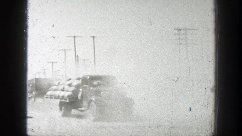 A loaded vintage truck drives through dust on a rural California road, with utility poles receding into the background.
