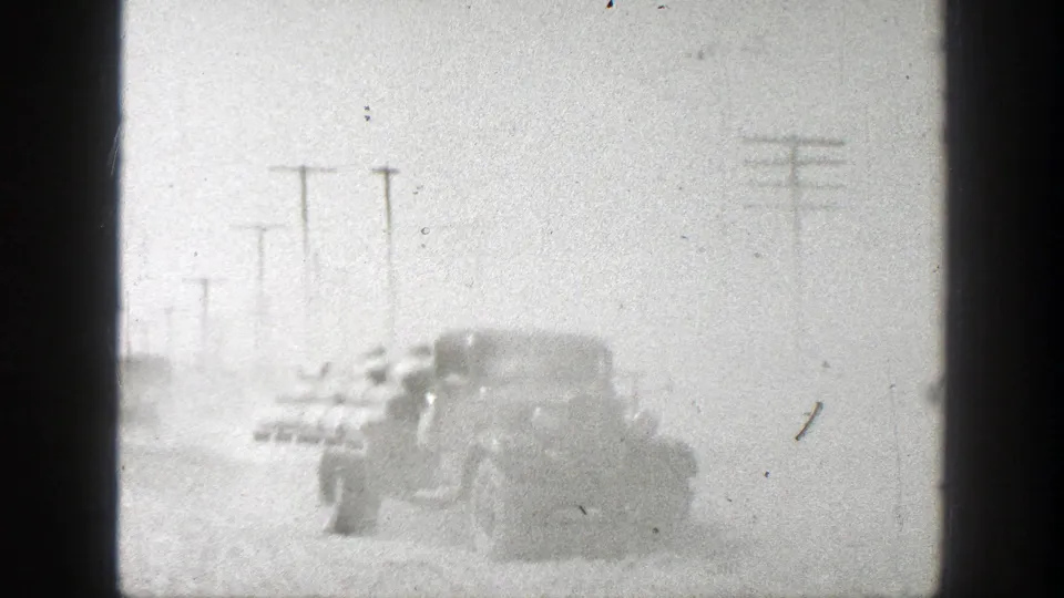 The cargo truck continues away on the dusty 1939 California road, its load partly visible through the film haze.
