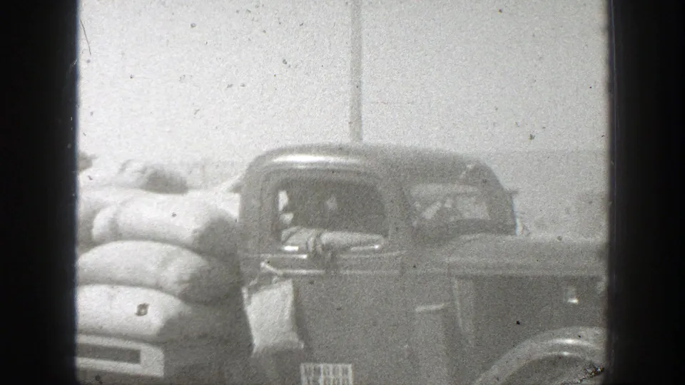Close 1939 California frame of a loaded vintage truck with cargo sacks and an occupant visible through the cab window.