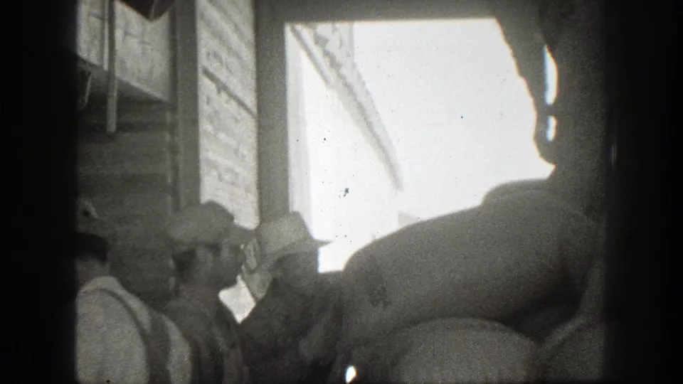 1939 California 8mm frame showing men in period workwear handling large sacks near a loading dock or doorway.