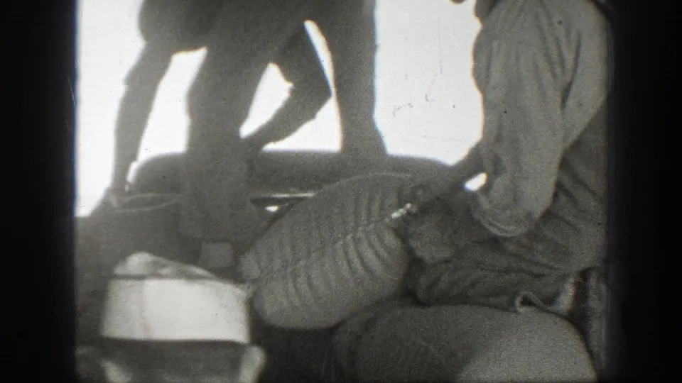 In 1939 California footage, adult men in work clothes gather closely around a large heaped sack as one handles the opening.