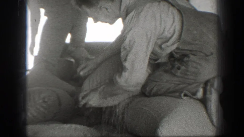Men in work clothing gather tightly around a large sack in the 1939 California home-movie frame, with hands visible near the opening.