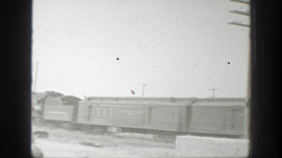 Black-and-white 1939 California frame showing passenger rail cars moving or standing along tracks in an open rail setting.