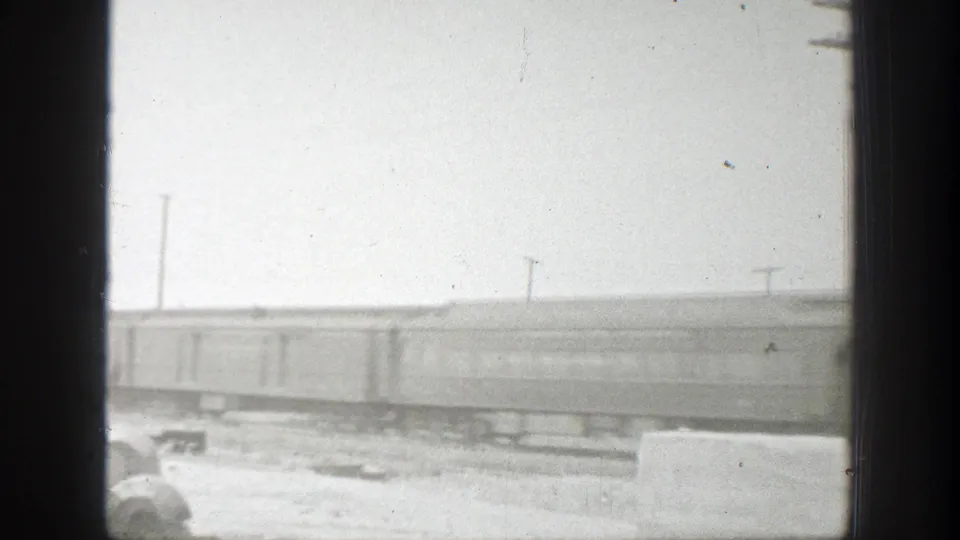 1939 California home-movie frame of passenger train cars passing a window-framed view, with tracks and utility poles behind them.