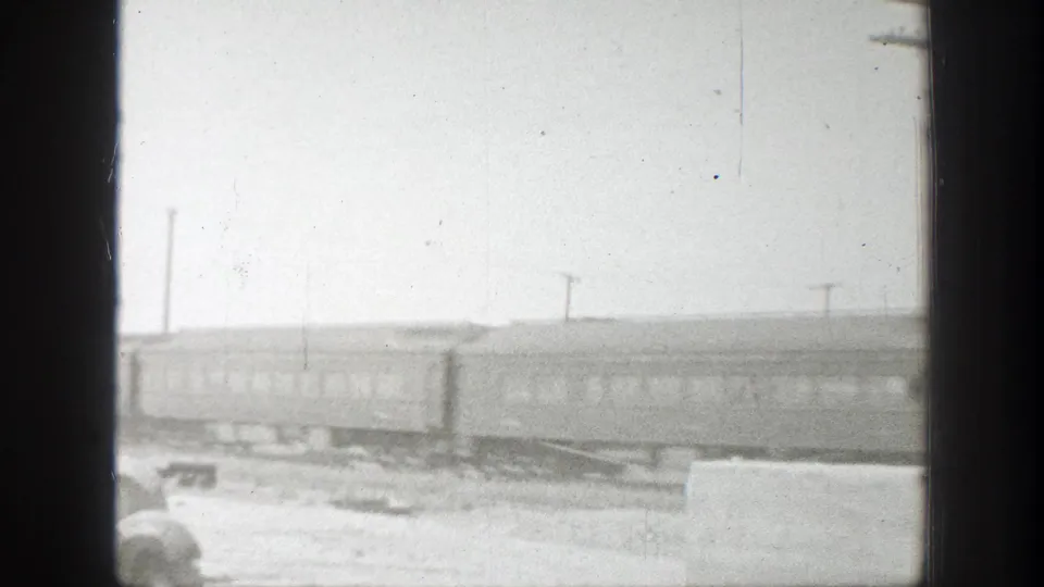 Black-and-white 1939 California 8mm frame showing passenger train cars moving across open rural ground with utility poles in the background.