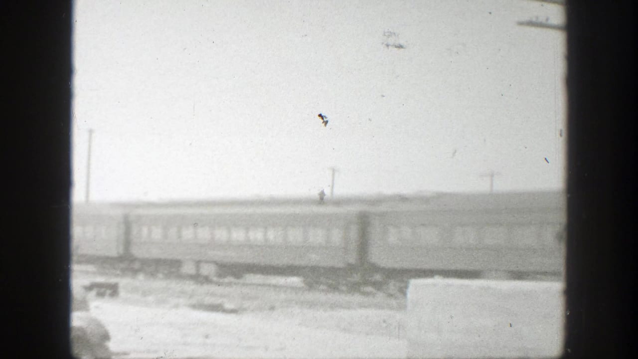 Passenger cars continue along the track under a pale sky.