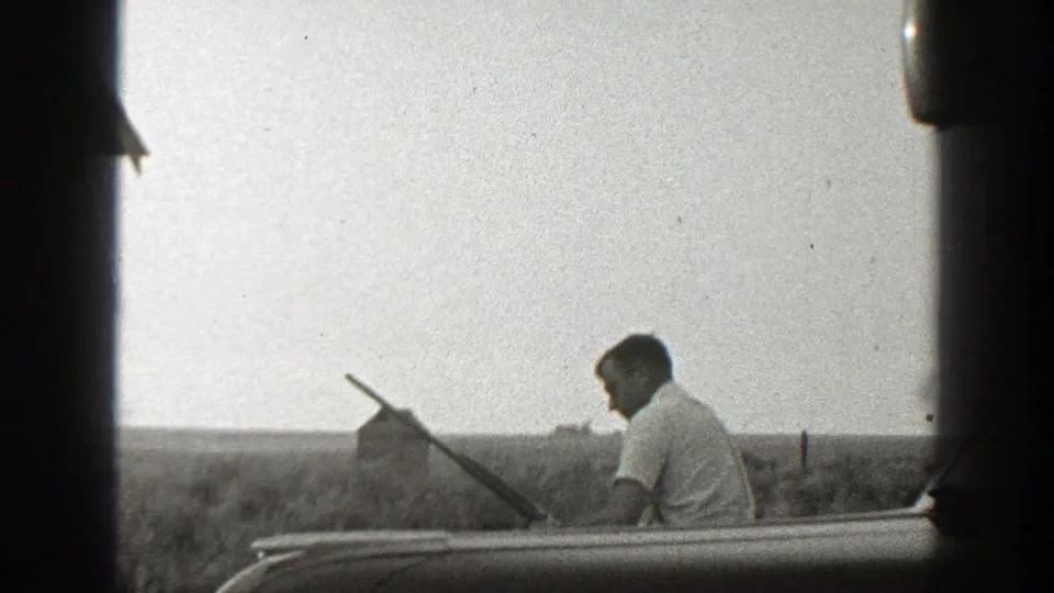 The 1939 California frame shows a man carrying a long gun across a rural field, with vehicle framing and a small distant structure visible.