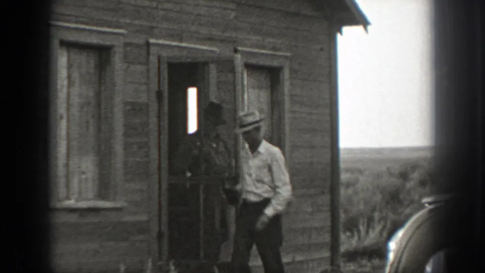In 1939 California home-movie footage, adult men in hats and shirts gather at the doorway of a rustic wooden building.