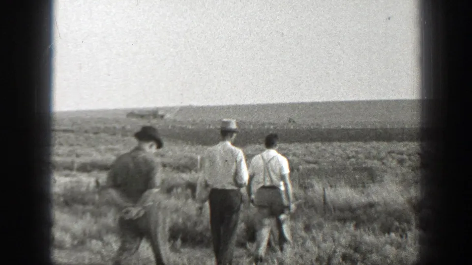 Three adult men walk through a dry California field in 1939 home-movie footage, dressed in hats, light shirts, and trousers.