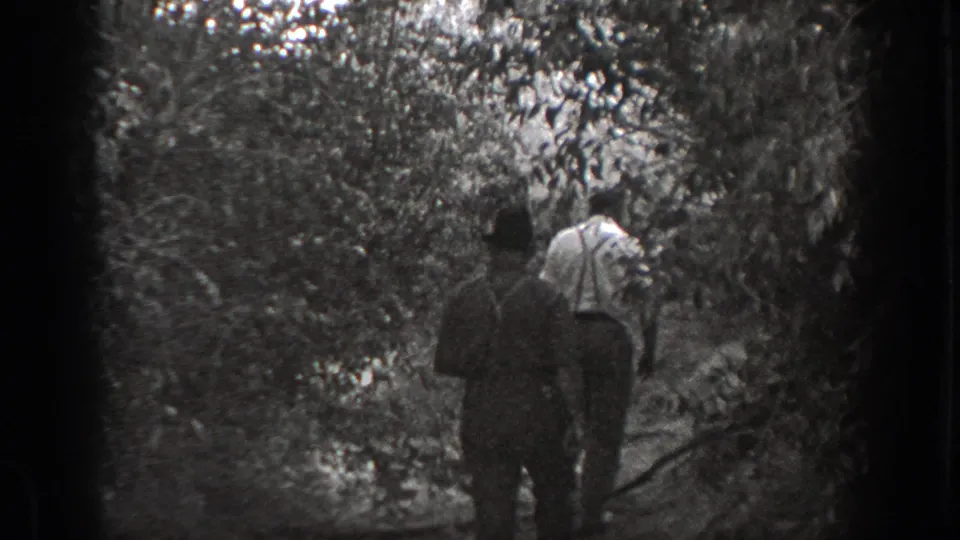 Black-and-white 1939 California frame showing two men from behind as they move through dense trees and undergrowth.