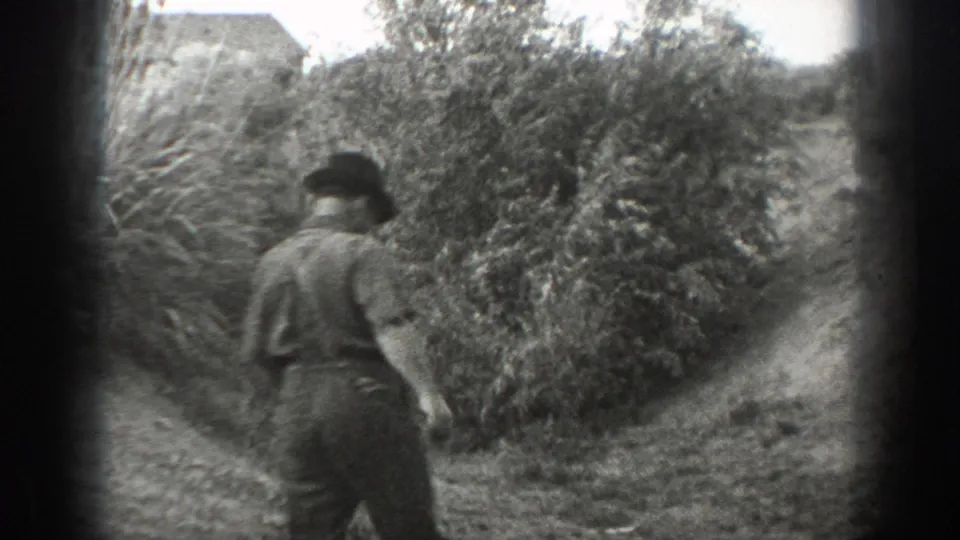 An adult man in dark trousers walks away along a narrow path beside dense bushes in 1939 California 8mm home-movie footage.