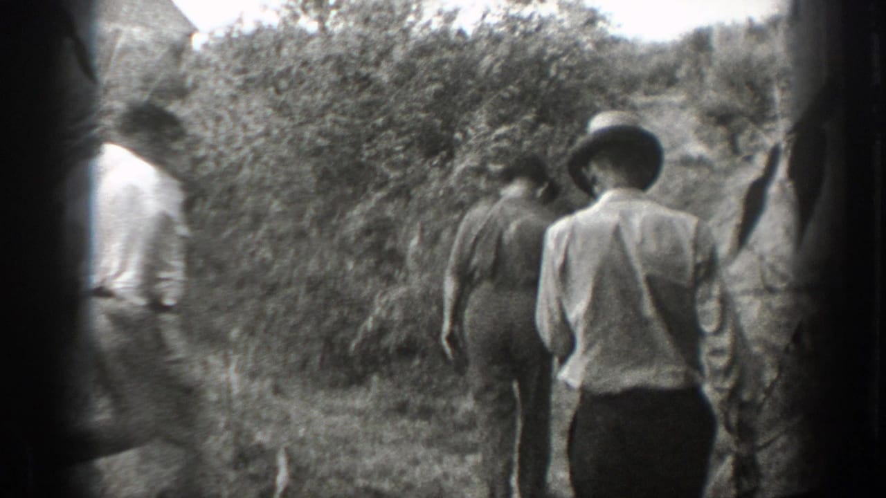 In 1939 California home-movie footage, men in light shirts walk away along a narrow brush-lined path.