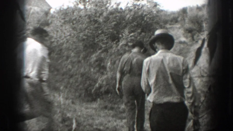 In 1939 California home-movie footage, men in light shirts walk away along a narrow brush-lined path.