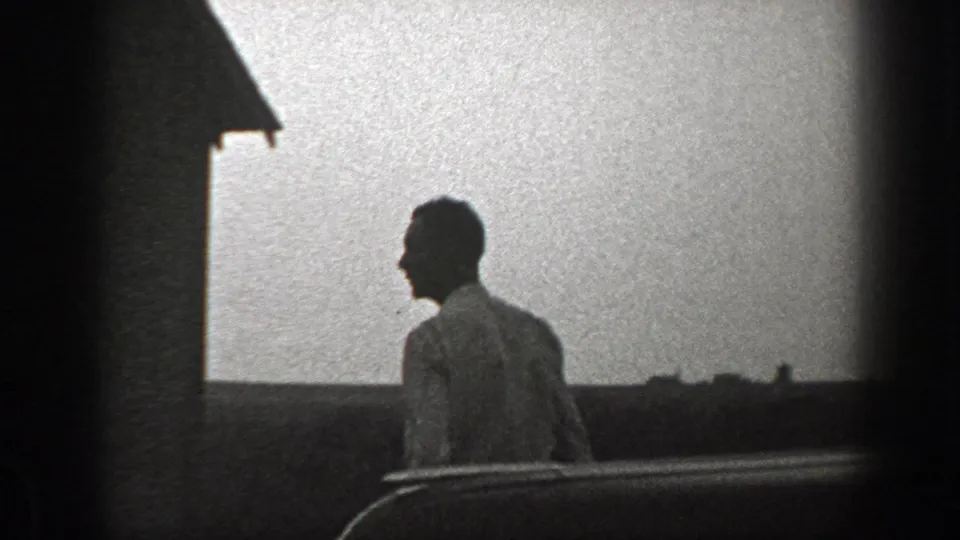 A man in a white shirt passes in profile near a bright exterior wall, likely beside the rural shack in the 1939 California clip.