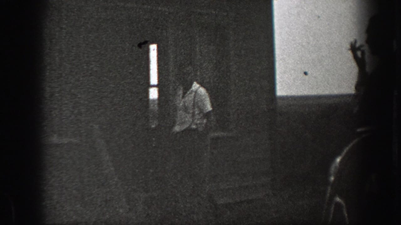 Man in a light shirt near exterior steps, with a bright strip and dark foreground obstruction.